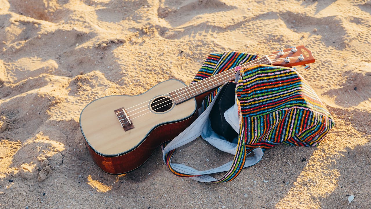 gallery-02 A ukulele rests next to a colorful bag on a sunny beach, capturing a peaceful summer vibe.